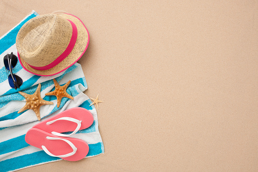 Beach accessories: pink flipflop, straw hat, towel and sunglasses isolated on sand.