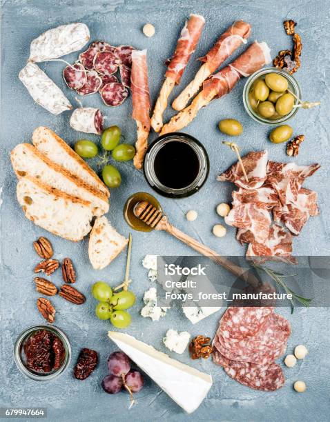 Cheese And Meat Appetizer Selection Or Wine Snack Set Variety Of Cheese Salami Prosciutto Bread Sticks Baguette Honey Grapes Olives Sundried Tomatoes Pecan Nuts Over Grey Concrete Textured Backdrop Top Vie Stock Photo - Download Image Now