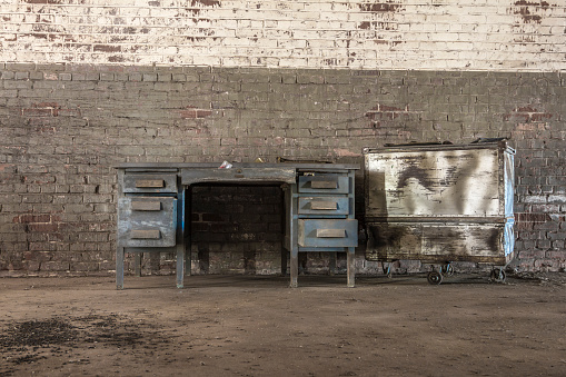 Empty desk and a metal case against a brick wall in an abandoned factory
