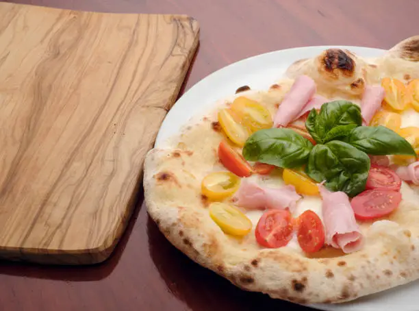 wonderful Italian pizza placed on a table near an empty olive-wood cutting board