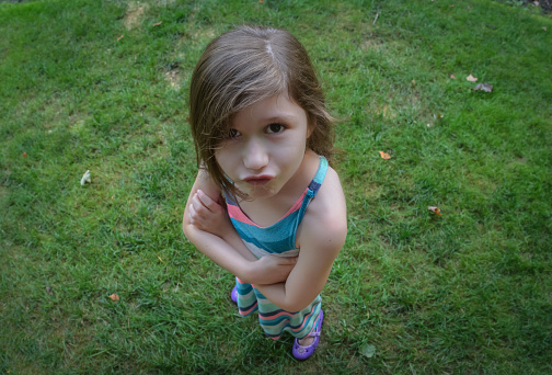 View from above of a young girl looking up at the camera with her arms folded and a defiant look on her face.