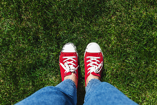 Legs in old red sneakers on green grass. View from above. The concept of youth, spring and freedom.