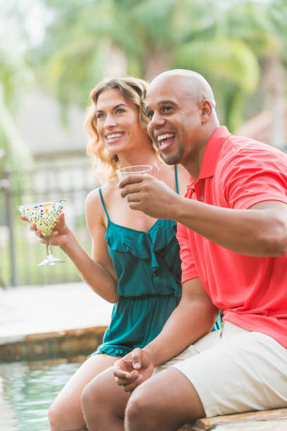 istock Interracial couple drinking cocktails on pool deck 679991172