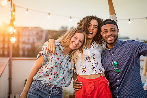 Portrait of happy multi ethnic friends enjoying on terrace. Smiling man and women are celebrating together during sunset. They are wearing casuals in party.