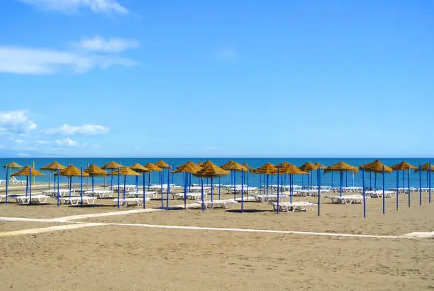 Summer holiday view of a Mediterranean beach prepared for a tourist season, a sandy beach by the blue sea, deckchairs, straw umbrellas and a wooden path at Torremolinos resort on Costa del Sol, Spain.