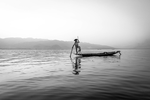 Fisherman trying to catch fish during early morning at famous Inle lake of Myanmar in his wooden boat.