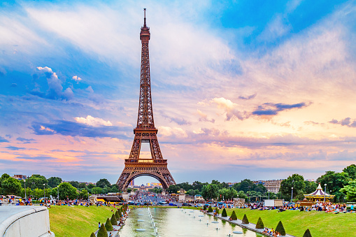 Eiffel tower, view from Trocadero park over fountain. People making their evening promenade around fountain. Eiffel tower is famous symbol of Paris city and France. Sunset scenery, epic dramatic sky.