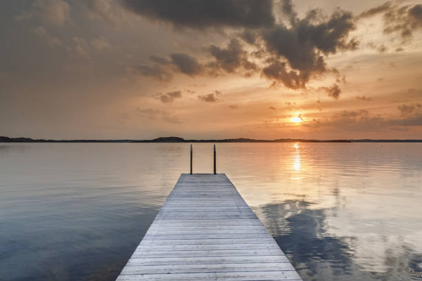 istock Beautiful glowing orange sunset over a rustic timber plank jetty reflected in calm waters of the sea below, a background of natural beauty and serenity. Northern sea, Sweden, Scandinavia. 680093230