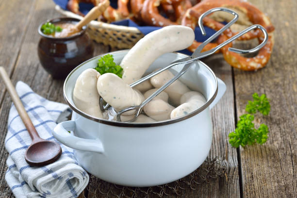Bavarian white sausages in hot water Hot Bavarian white sausages in an enamel cooking pot served on a wooden table with fresh pretzels and sweet mustard weisswurst photos stock pictures, royalty-free photos & images