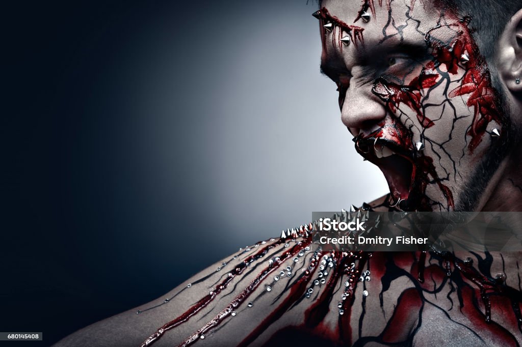 Bleeding scars. A creepy halloween concept of a screaming moor in pain with a piercing and bloody body art. Adult Stock Photo