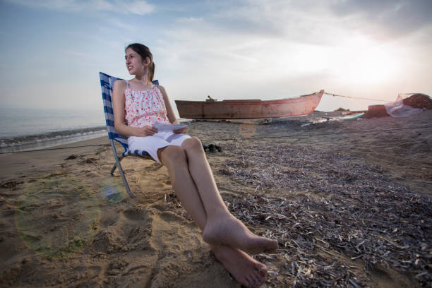 młoda kobieta o zachodzie słońca siedząca na leżaku na plaży - sunset beach sky heat zdjęcia i obrazy z banku zdjęć
