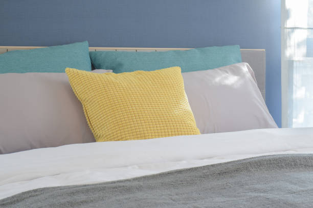 istock Yellow, light gray and green pillows setting on bed in modern interior bedroom 680177734