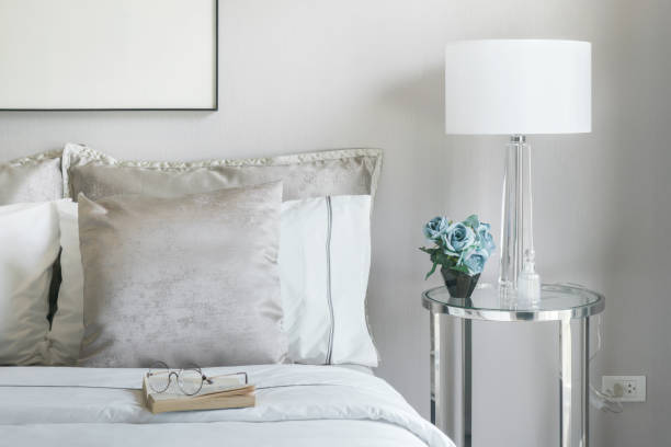 istock Light gray and white pillows on bed with flower jar on bedside table 680177948