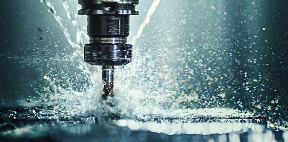 Closeup shot of a CNC machine processing a piece of metal. There are three water streams splashing the object to cool it down.