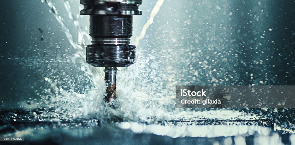 CNC machine drill. Closeup shot of a CNC machine processing a piece of metal. There are three water streams splashing the object to cool it down. CNC Machine Stock Photo