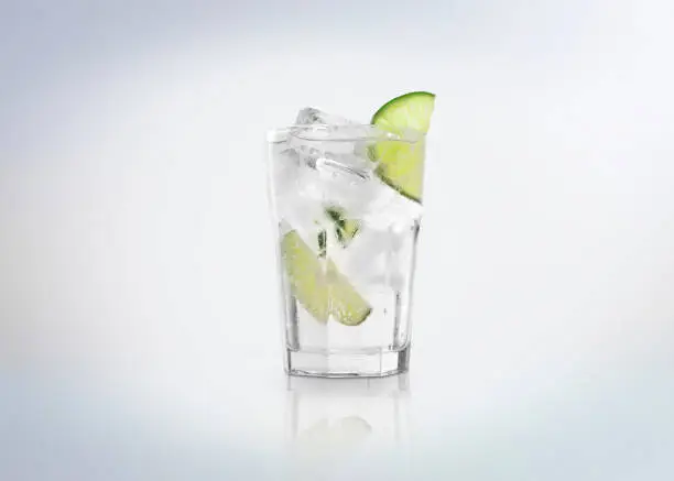 Photo of A glass of Gin Tonic cocktail  drink with ice cubes (on the rocks) and a slice of lime.