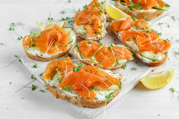 istock Smoked salmon bruschettas with soft cheese and cucumber shavings on white board. 680224106