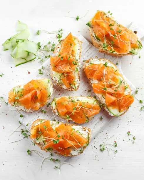 Smoked salmon bruschettas with soft cheese and cucumber shavings on white board