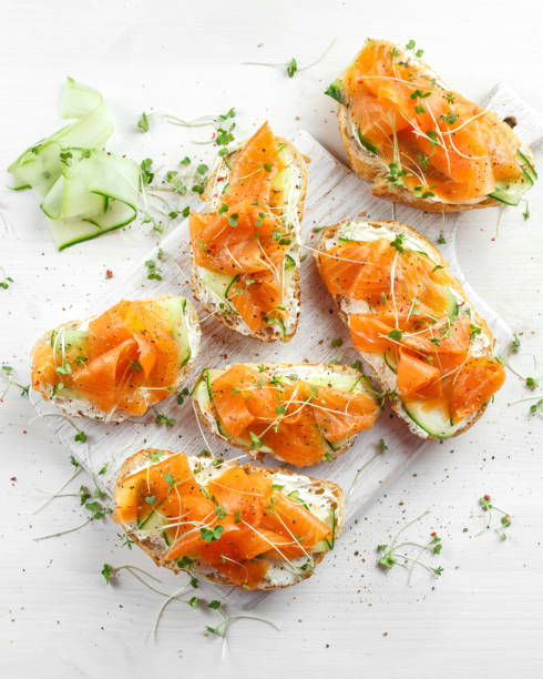 smoked salmon bruschettas with soft cheese and cucumber shavings on white board. - crostini imagens e fotografias de stock