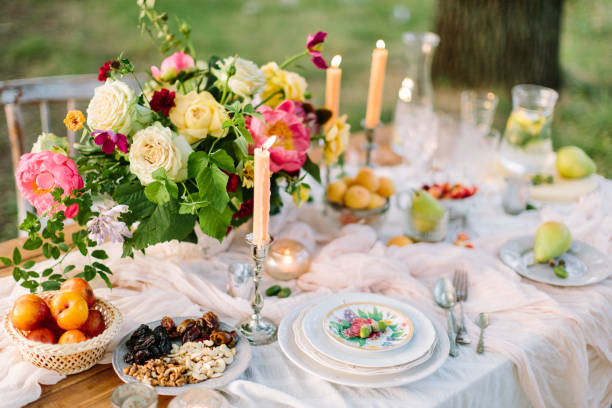 istock picnic, summer, holiday concept - beautiful table setting at the green lawn with tree, openwork white tablecloth, colorful summer bouquet of peony and roses, fruits, candlesticks, glassware, lemonade 680227300