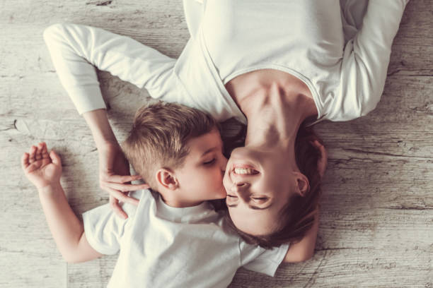 Mom and son Top view of beautiful woman and her cute little son smiling while lying on the floor. Boy is kissing his mom in cheek cheek photos stock pictures, royalty-free photos & images