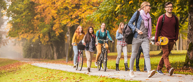 Group of students moving through the park, most are walking and two are riding their bicycles.