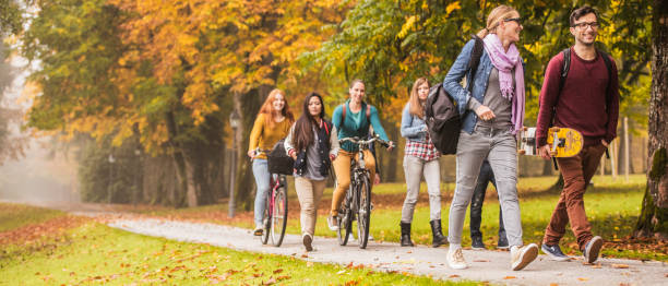 panoramic photo of students walking through the park - campus life imagens e fotografias de stock