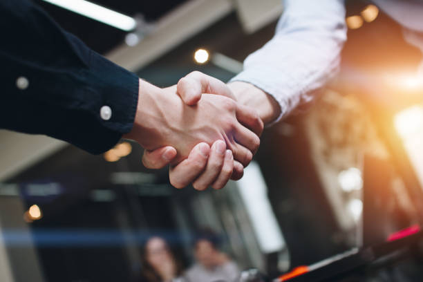 Bussines partners handshakes in modern open space on the background of coworking team on new startup project Bussines partners handshakes in modern open space on the background of coworking team on new startup project casual handshake stock pictures, royalty-free photos & images