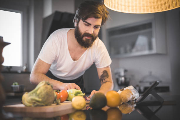 istock Young bearded man cutting vegetable in the kitchen and reading recipe on digital tablet 680327764