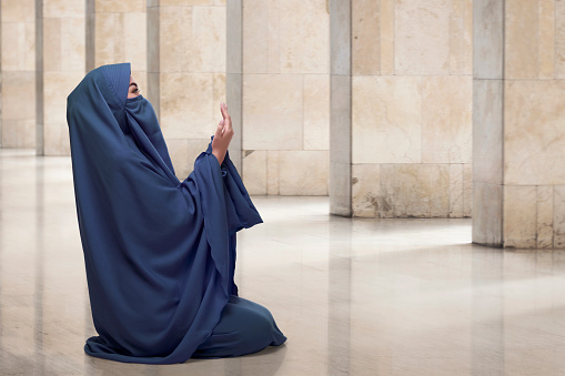 Religious asian muslim woman wearing face covering praying in the mosque