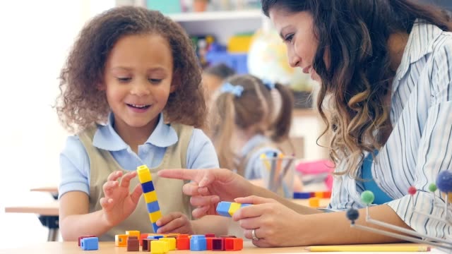 Adorable mixed race kindergarten student counts with counting cubes