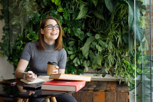 mujer creativa sonriendo mientras mira a la ventana - setting goals fotografías e imágenes de stock