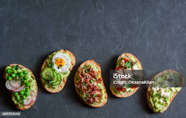 Breakfast Avocado Sandwich With Crispy Bacon Quail Egg Tomatoes Goat Cheese Green Peas Radish Cucumber Healthy Snack On A Dark Background Top View Copy Space Stock Photo - Download Image Now