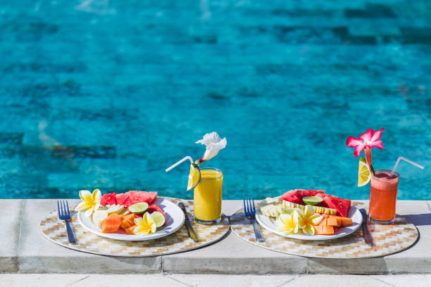 istock Two plates with fresh fruit and two juice with slice orange. Healthy breakfast on poolside in hotel. Plate with papaya, pineapple, watermelon, lime. 680384588