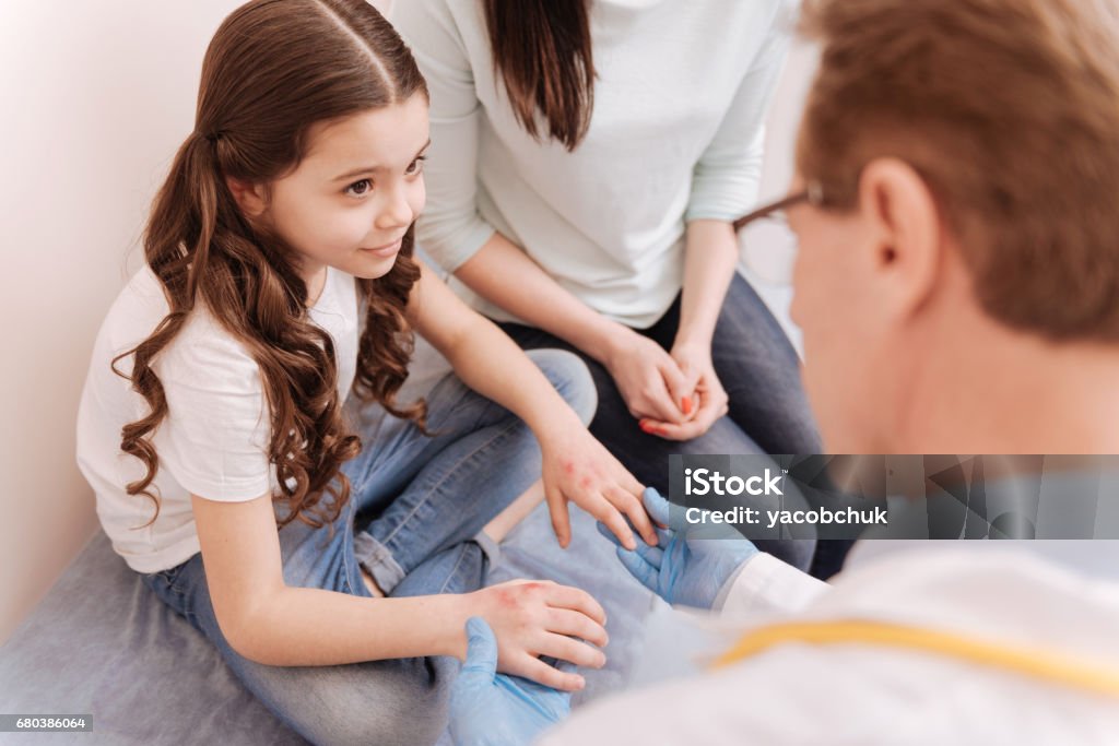 Pretty smart girl listening to experts instructions You should not scratch these. Charming sad lovely child sitting at doctors office for showing her hands hearing what the specialist prescribing her Child Stock Photo