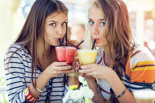 Teenage girlfriends drinking refreshing cold drinks and looking at camera