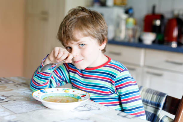 istock Adorable little school boy eating vegetable soup indoor. 680395896