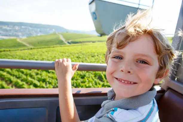 Smiling happy blond littlekid boy in cable funicular over vineyards in summer or autumn. Cute child enjyoing the view. Germany, vineyard near Mosel and Rhine.