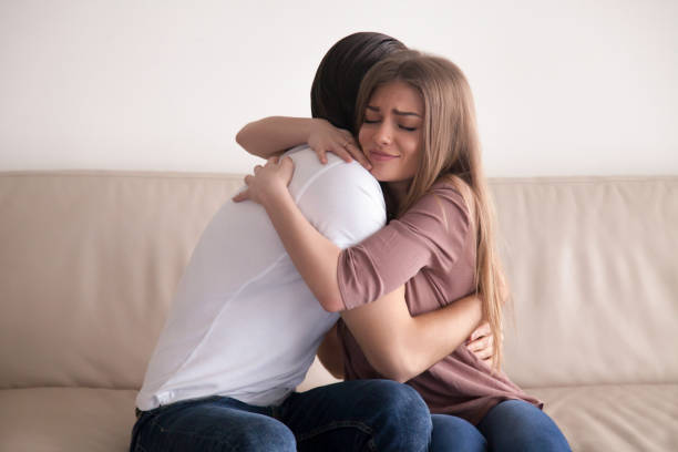 Portrait of young couple hugging tight sitting on couch indoors Portrait of emotional young couple hugging each other tightly, boyfriend and girlfriend embracing sitting on couch, reconciliation after argument, love you so much, strong affection in relationships mercy hug stock pictures, royalty-free photos & images