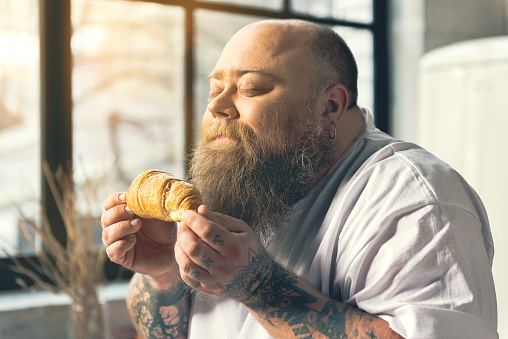 What wonderful smell. Fat bearded guy is enjoying scent of fresh baked pastry. His eyes are closed with pleasure