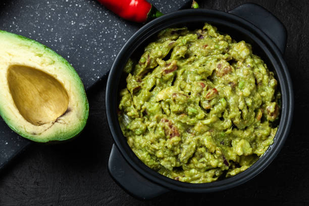 Bowl of guacamole with fresh ingredients Bowl of guacamole with fresh ingredients on a black table guacamole restaurant mexican cuisine avocado stock pictures, royalty-free photos & images