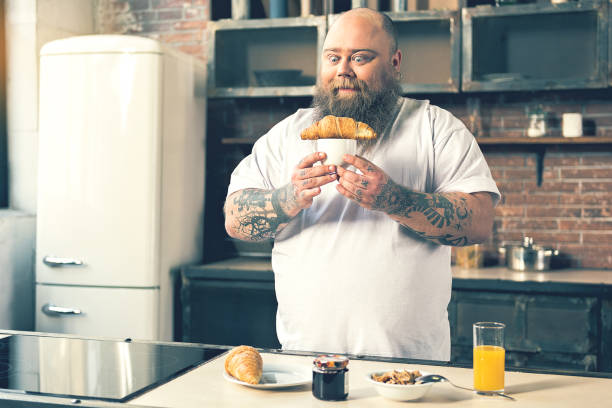 istock Starving fat man having breakfast in cook room 680412442