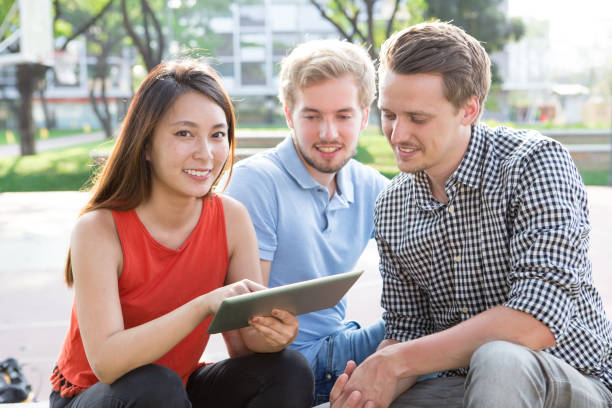 Positive Asian woman using tablet with groupmates