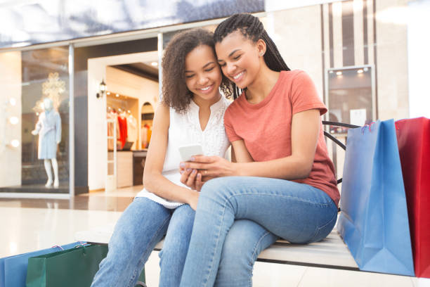 istock Two Smiling Black Girls Sitting on Bench in Mall 680431008