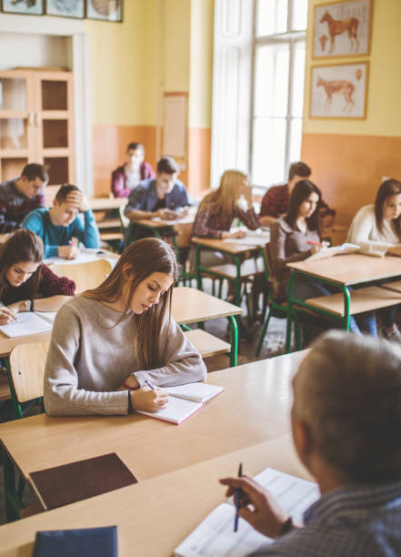 Selective focus backs of schoolchildren in class with teacher writing on the board