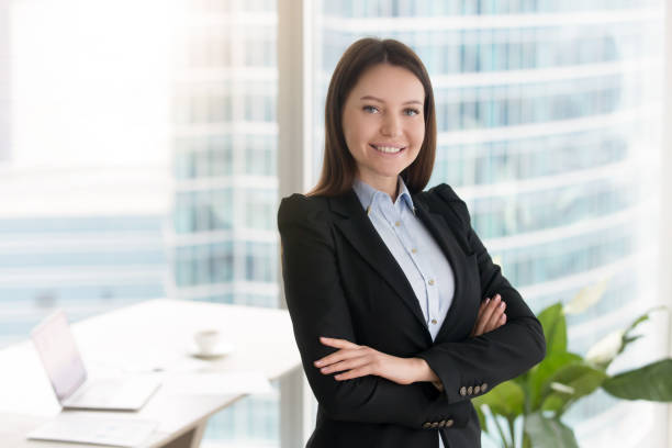 Young confident smiling businesswoman standing in office with arms crossed Portrait of young smiling businesswoman standing in modern office interior with arms crossed, looking at camera. Great career achievements, confident self-made woman and motivated professional application form photos stock pictures, royalty-free photos & images