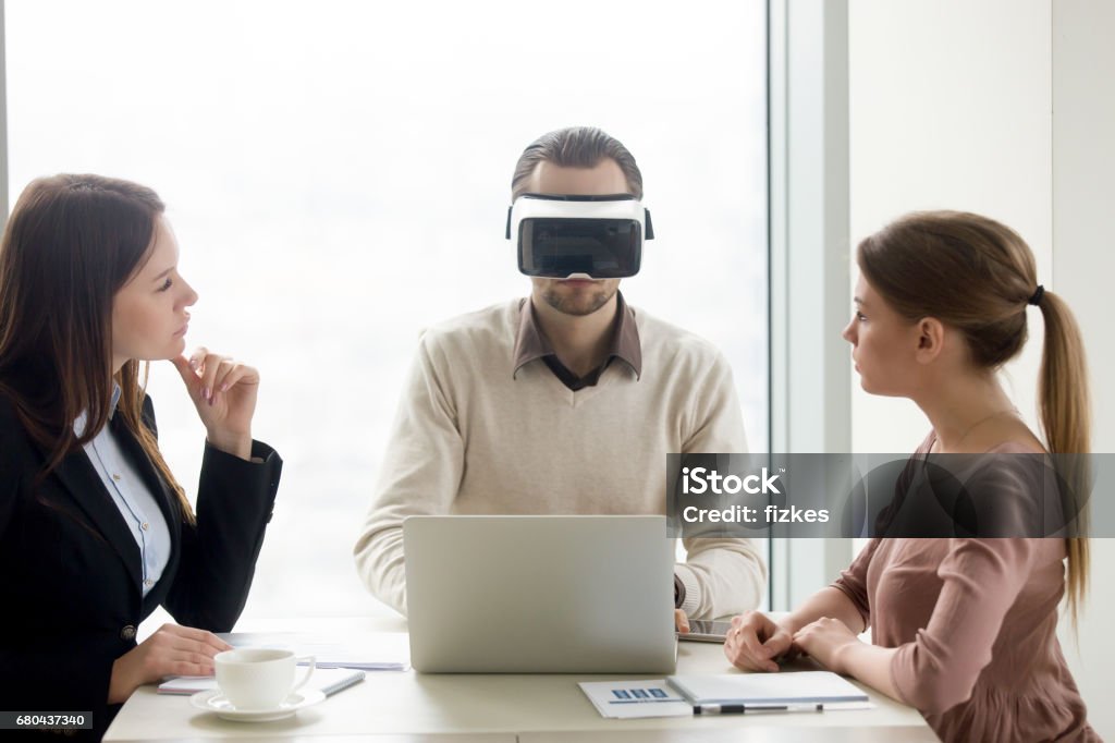 Man wearing VR headset, team developing virtual reality glasses software Businessman wearing innovative vr headset for laptop at business meeting. Business team developing virtual reality applications, future realistic technology on computer for business concept Adult Stock Photo