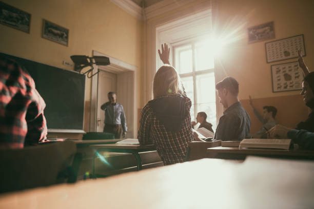 High school students raising hands during the lecture in classroom. Female teenage student and her classmates raising hand to answer teacher's question in the classroom. teenage high school girl raising hand during class stock pictures, royalty-free photos & images