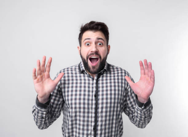 istock Young man with arms raised. Guy spread hands out. Isolated on white background. Bearded student wearing a white shirt arms opened looking up. 680445476