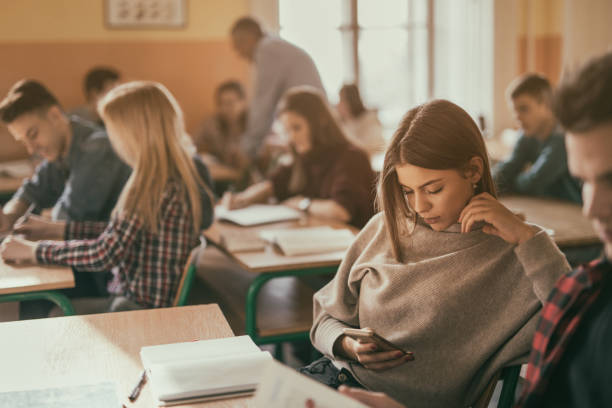 Teenage student texting on cell phone in the classroom. Female high school student using smart phone and text messaging while sitting in the classroom during the lecture. education student mobile phone university stock pictures, royalty-free photos & images